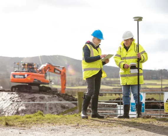 Engineers looking at tablet in Chattanooga TN with an orange back hoe tractor in the background