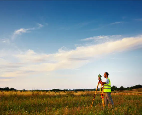 A man standing in a field with tools for Commercial Surveys in Davenport IA